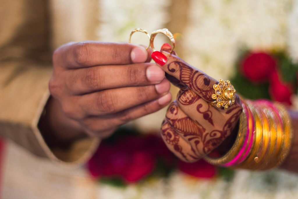 Close-up of hands with henna and jewelry during a traditional Indian wedding ceremony, exchanging rings.
