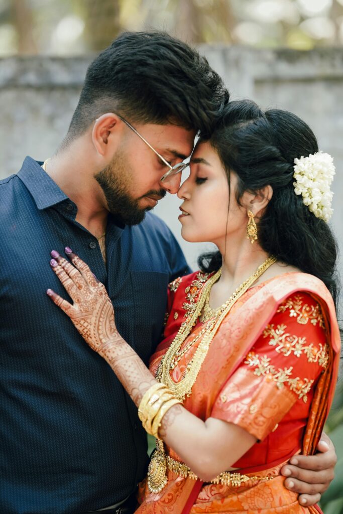 South Asian couple embracing, beautifully dressed in traditional Indian wedding attire outdoors.